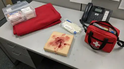 Matériel de simulation de blessure pour formation SST : compresse hémorragique, gants, téléphone d'alerte et trousse de secours